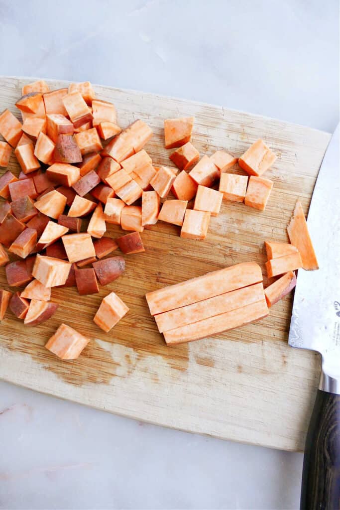 sweet potato being sliced into sticks and then cubes on a cutting board