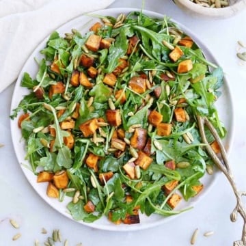 arugula sweet potato salad on a large serving dish with a spoon on a counter