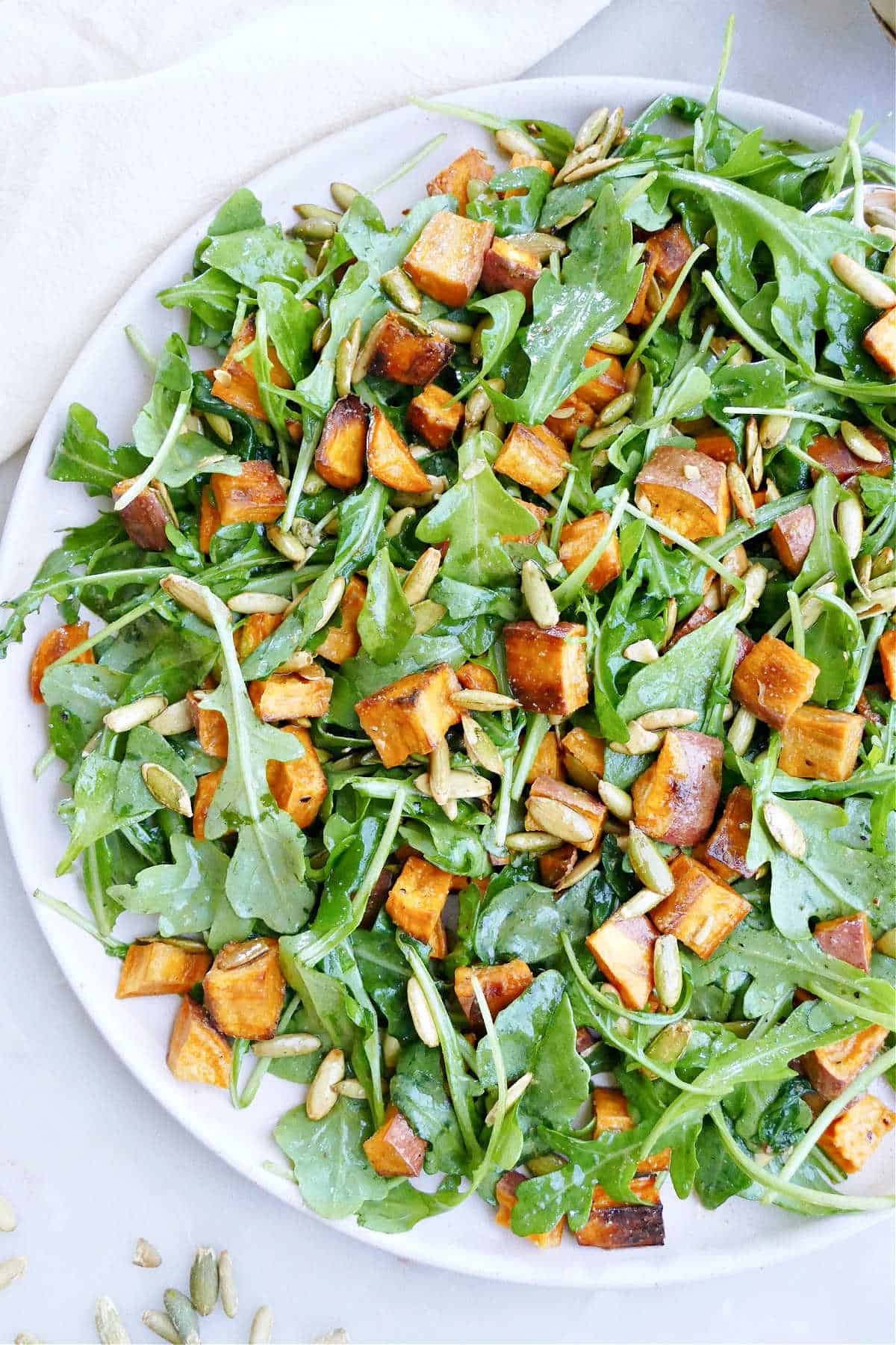 arugula sweet potato salad topped with pumpkin seeds on a large serving dish