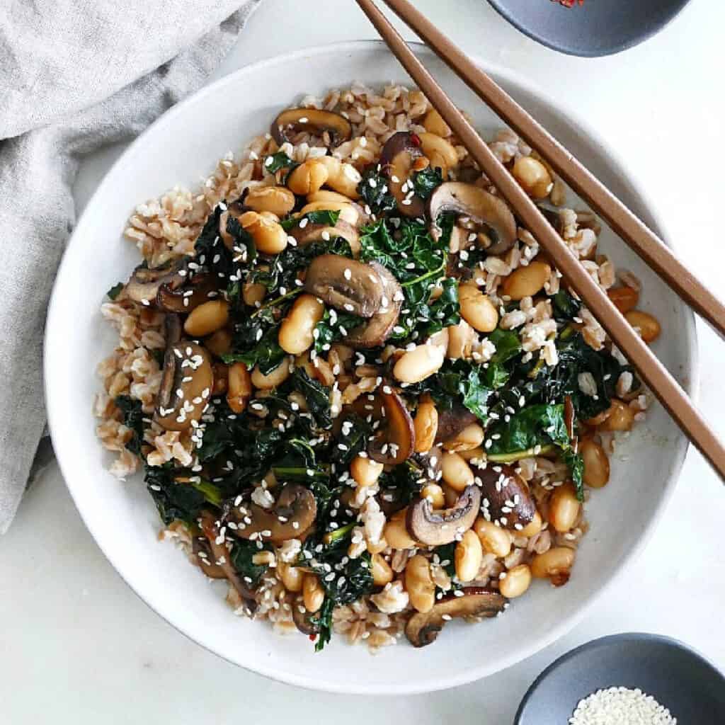 mushroom and kale stir fry on a plate with brown chopsticks
