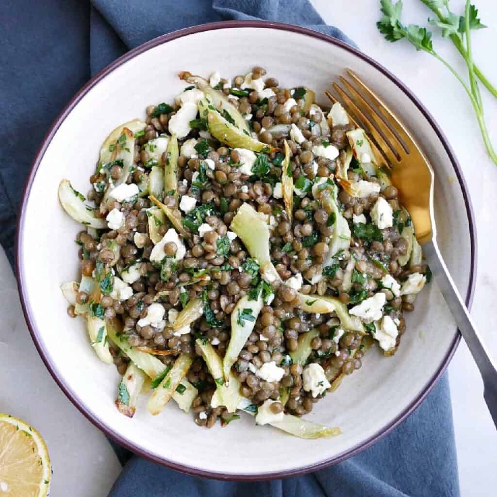 fennel lentil salad in a serving bowl with a fork on top of a napkin