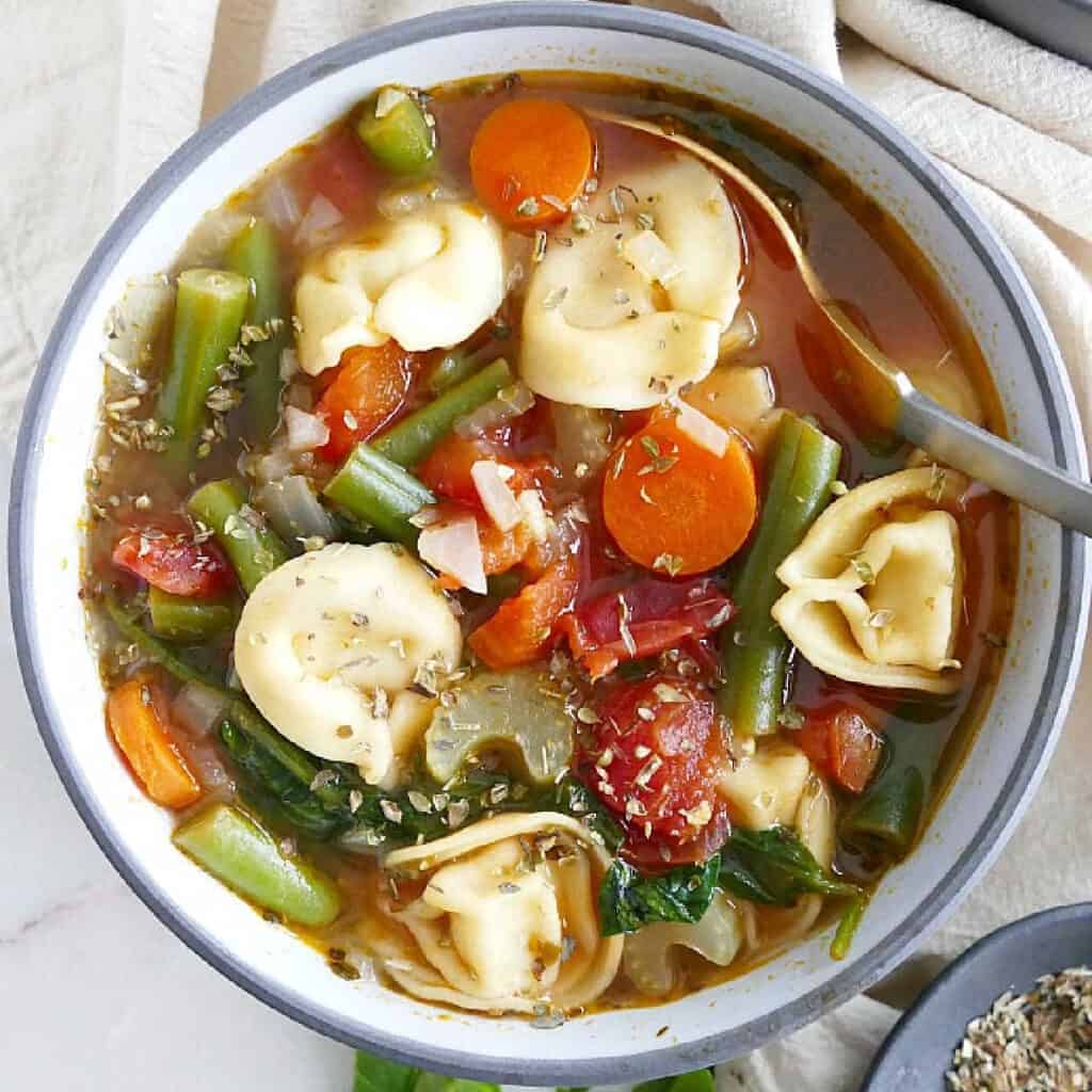 vegetable tortellini soup in a serving bowl with herbs and a spoon