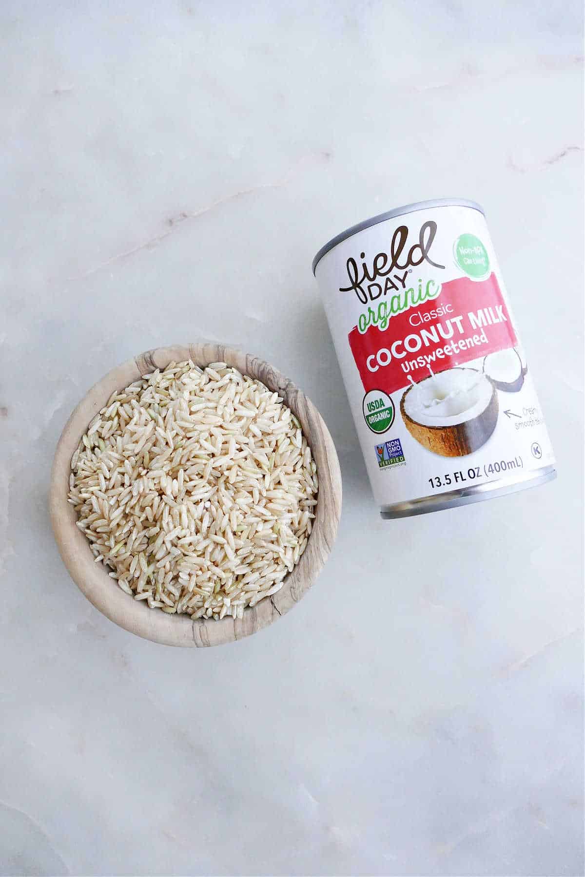 dry brown rice in a bowl next to a can of coconut milk on a countertop