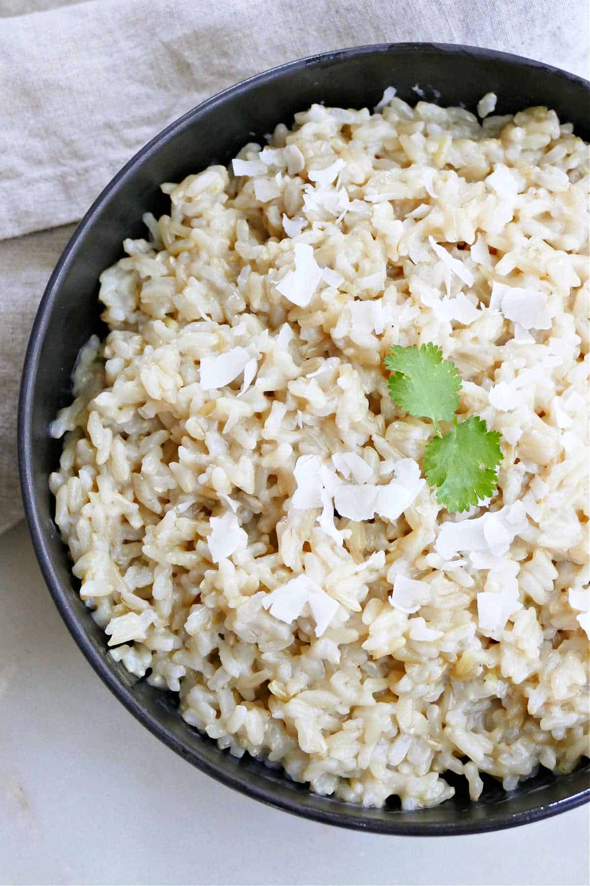 coconut brown rice in a bowl with cilantro leaves and coconut flakes