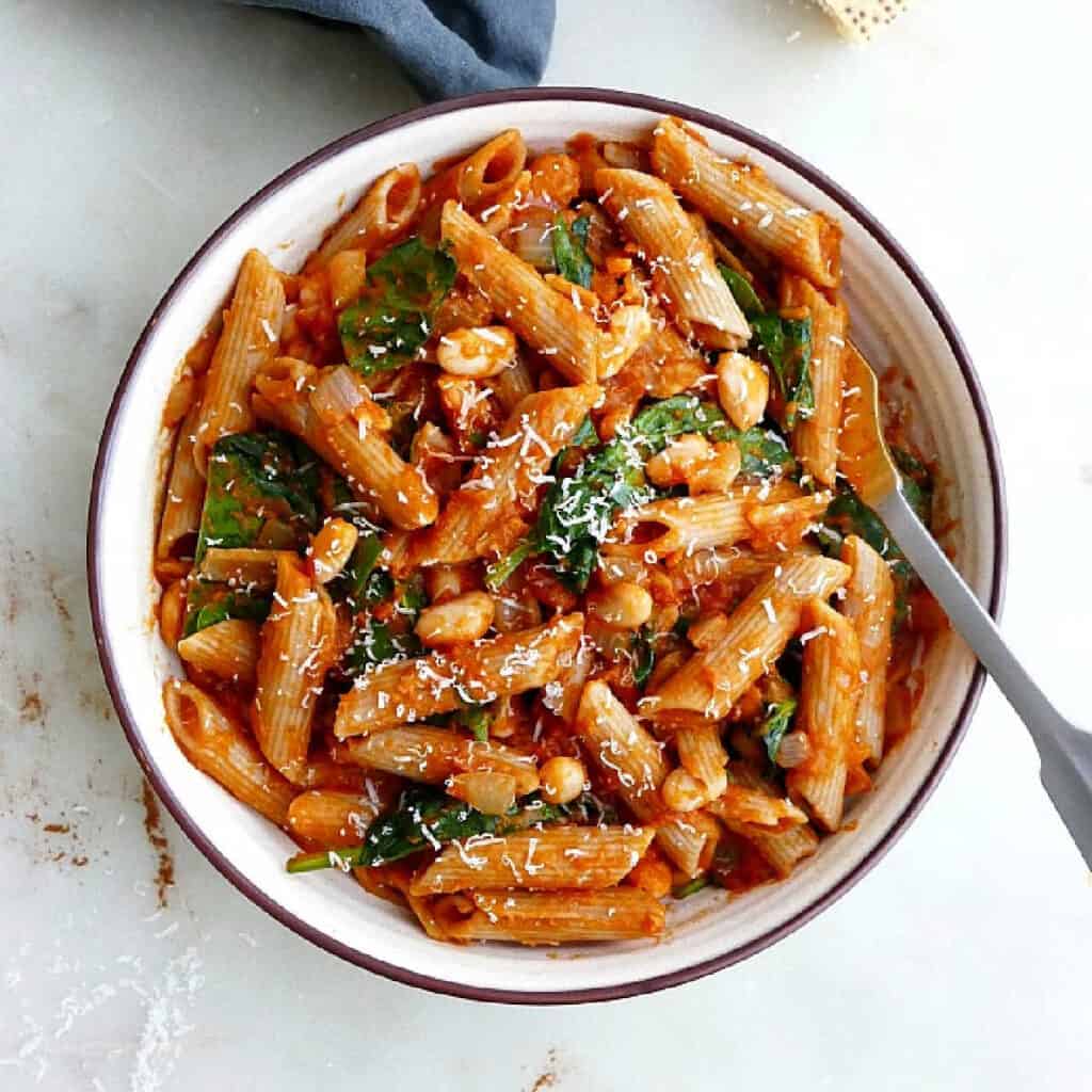 pumpkin tomato pasta with spinach and white beans in a serving bowl with a spoon