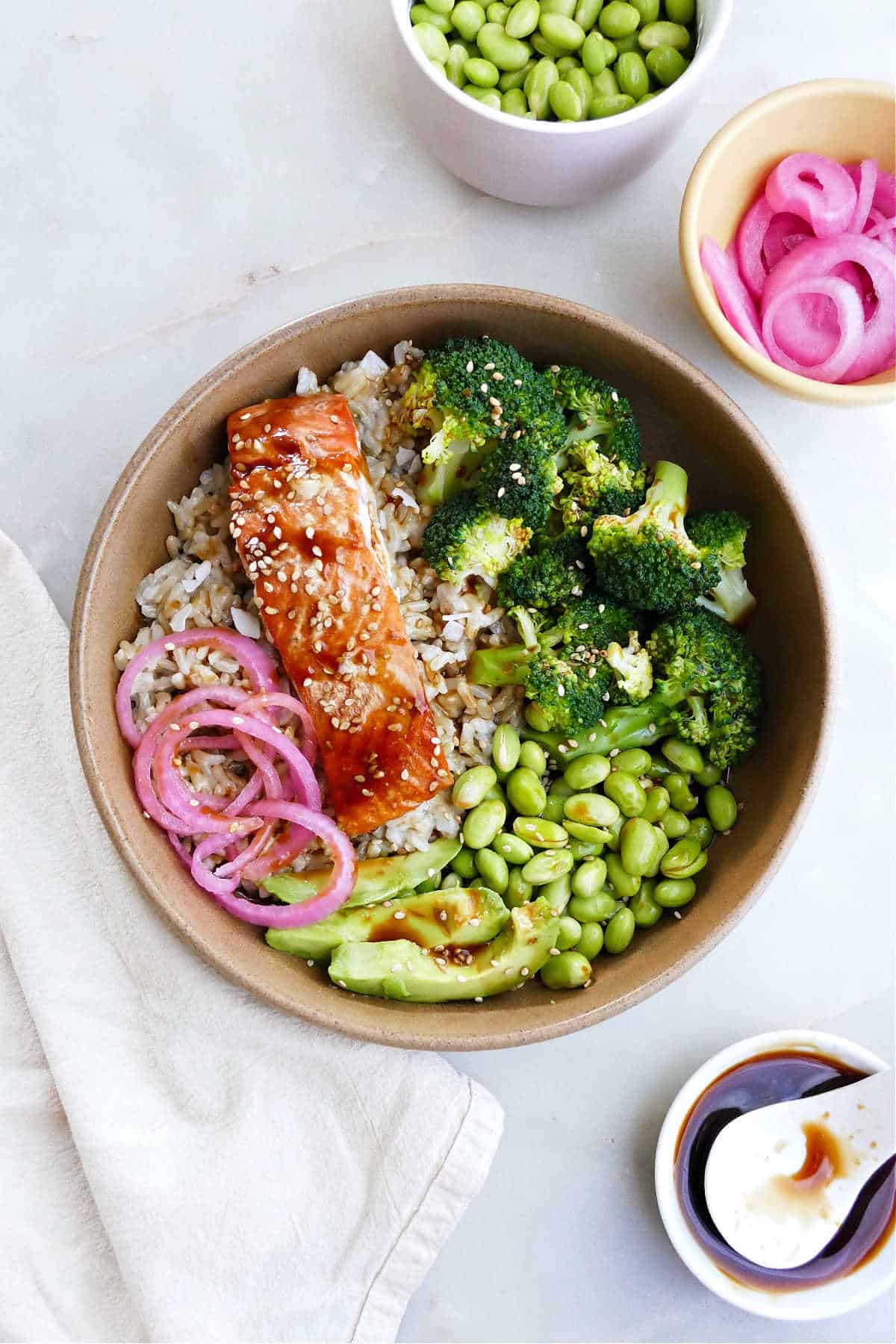 salmon teriyaki bowl topped with avocado and pickled red onions on a counter