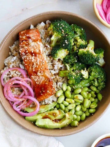 salmon teriyaki bowl topped with avocado and pickled red onions on a counter