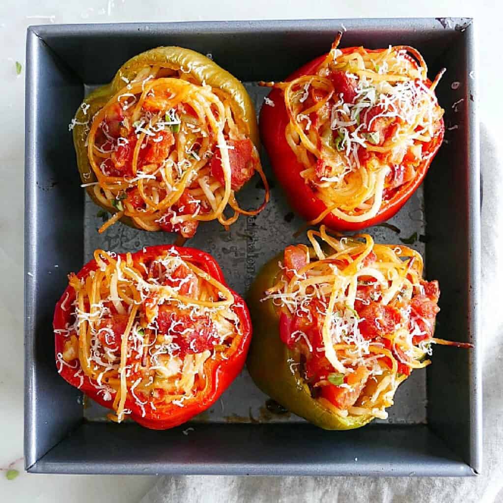 four spaghetti stuffed bell peppers in a baking dish