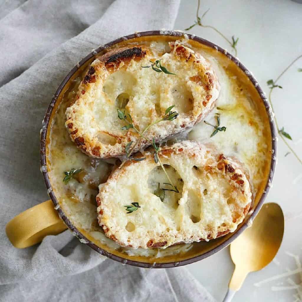 French onion soup with gruyere toasties in a serving bowl on a counter