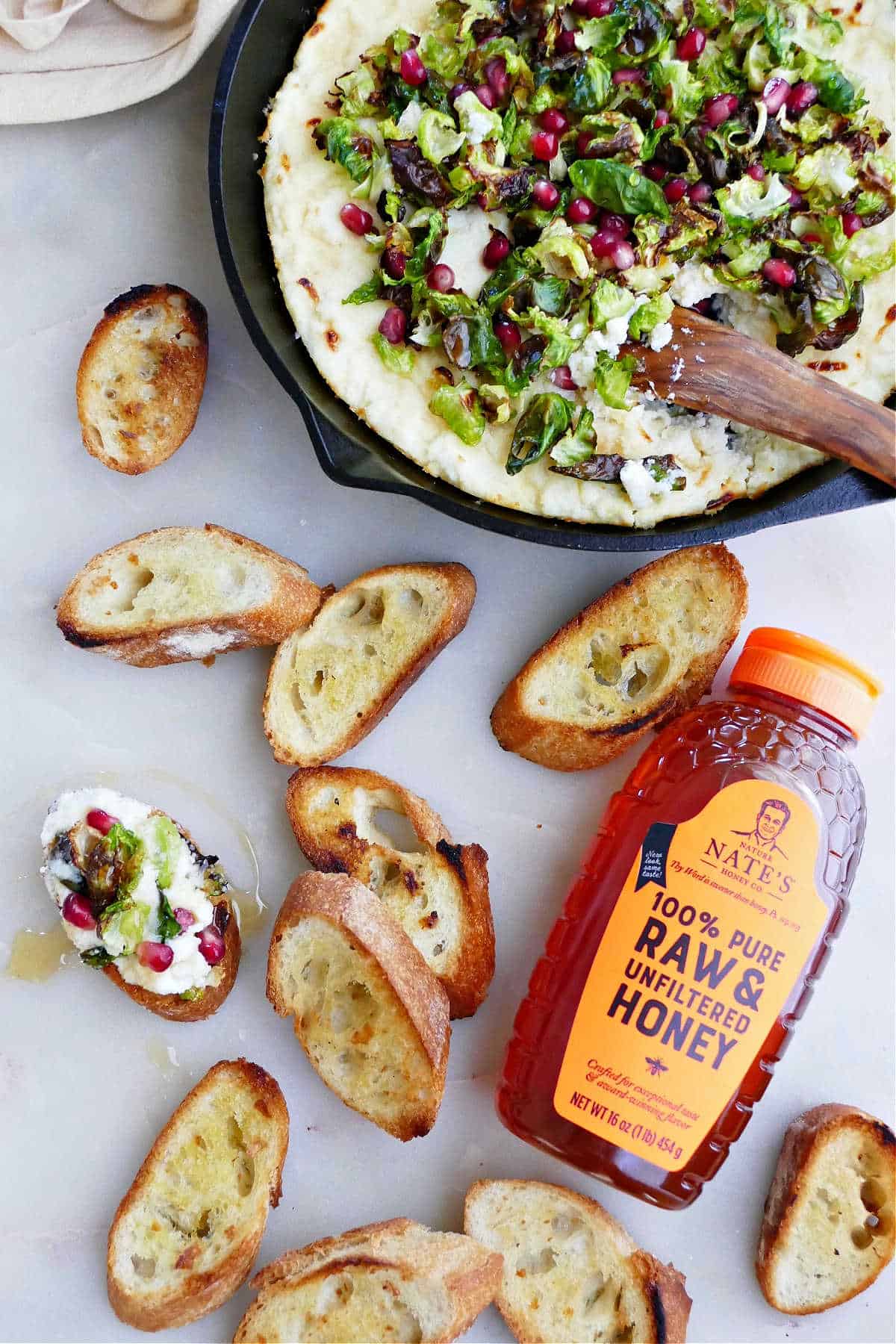 baked ricotta dip in a skillet with a knife next to baguette slices and a honey bottle