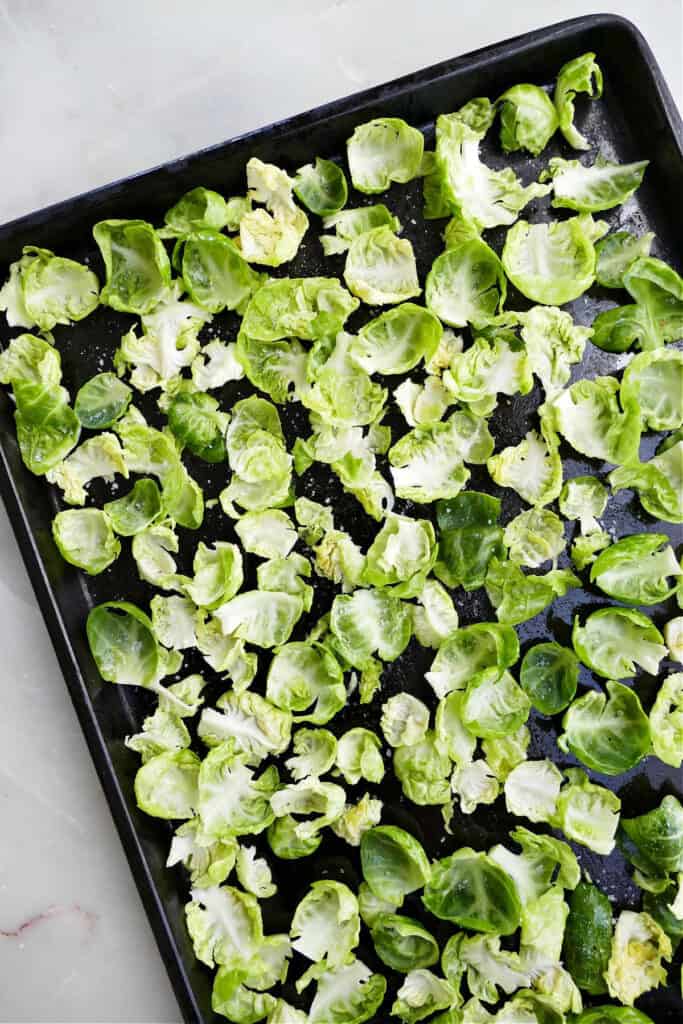 Brussels sprouts leaves spread out on a baking sheet tossed with oil