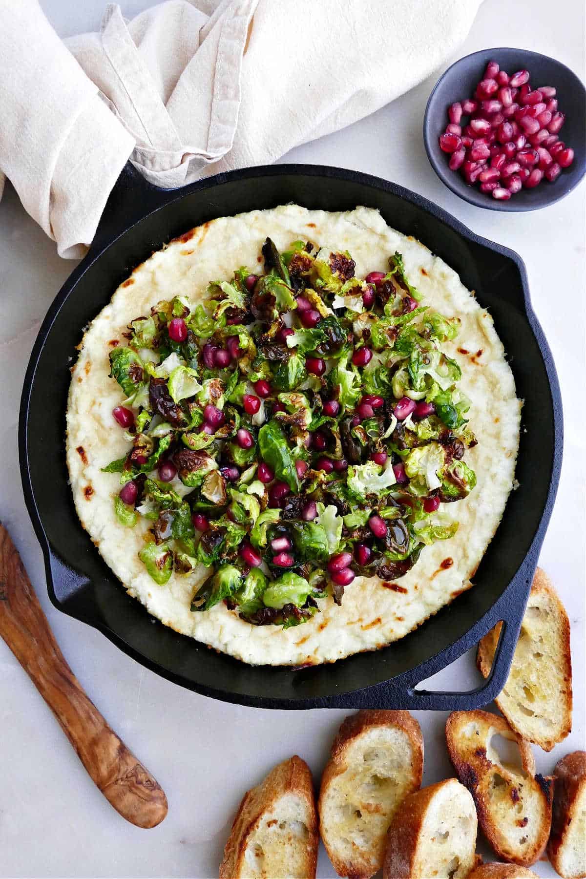 baked ricotta dip with Brussels sprouts and pomegranate topping in a skillet on a counter