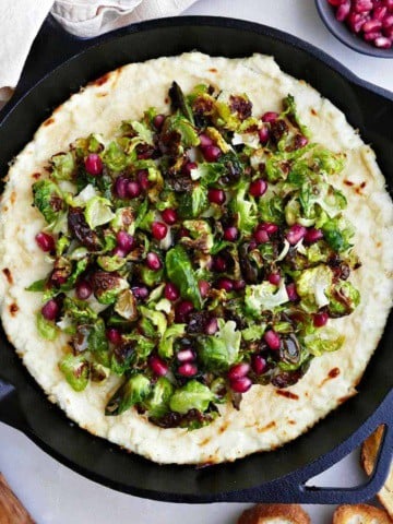 baked ricotta dip with Brussels sprouts and pomegranate topping in a skillet on a counter