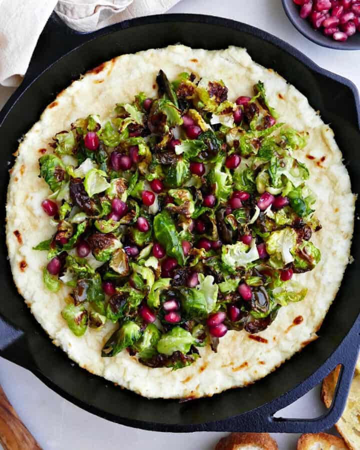 baked ricotta dip with Brussels sprouts and pomegranate topping in a skillet on a counter