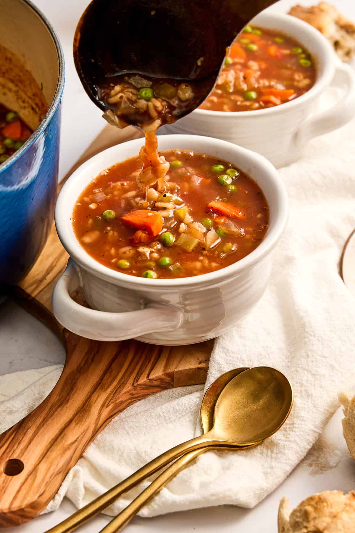 Barley soup being ladled into a bowl next to pot, napkin, and spoons.