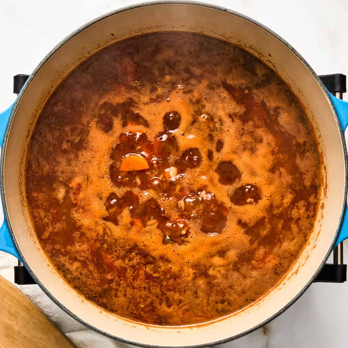 Barley soup with vegetables coming to a boil in a large pot.
