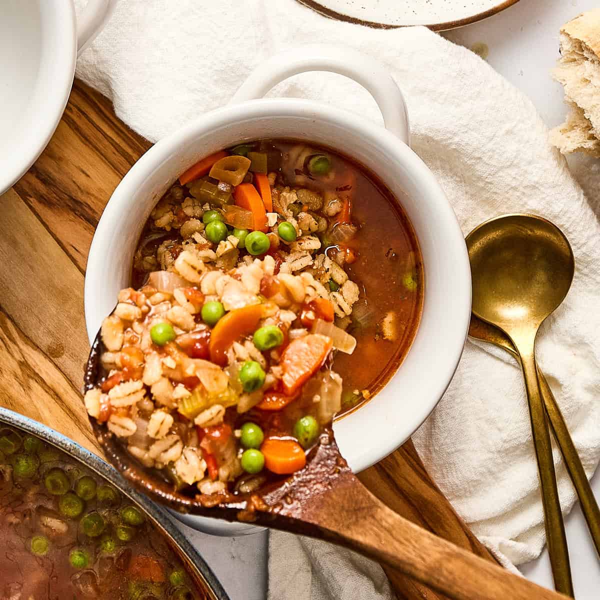 Woman ladling prepared vegetable and barley soup into a bowl for serving.
