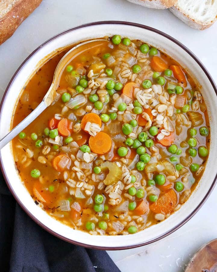 barley soup with vegetables in a serving bowl with a spoon next to bread