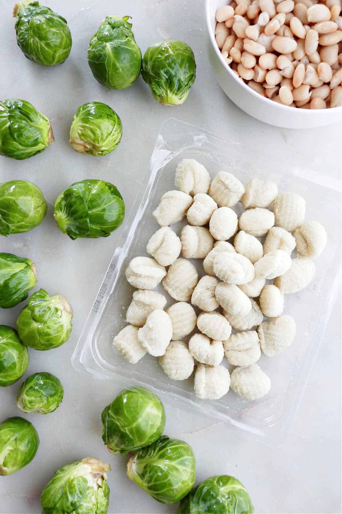 Brussels sprouts, gnocchi, and white beans spread out next to each other on a counter