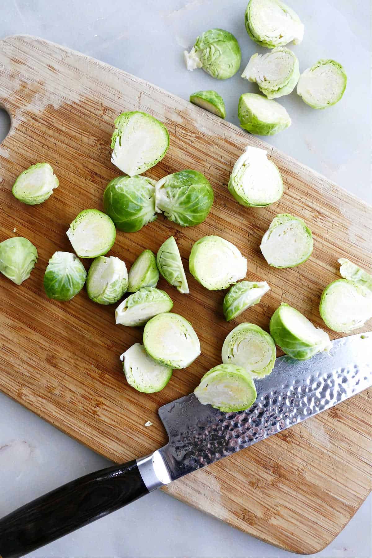 sliced Brussels sprouts on a bamboo cutting board next to a chef's knife