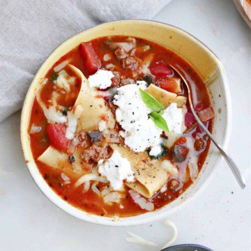 one pot lasagna soup in a serving bowl topped with ricotta cheese and basil