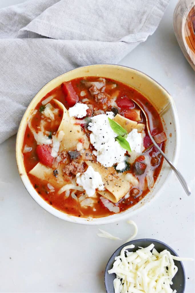one pot lasagna soup in a serving bowl topped with ricotta cheese and basil
