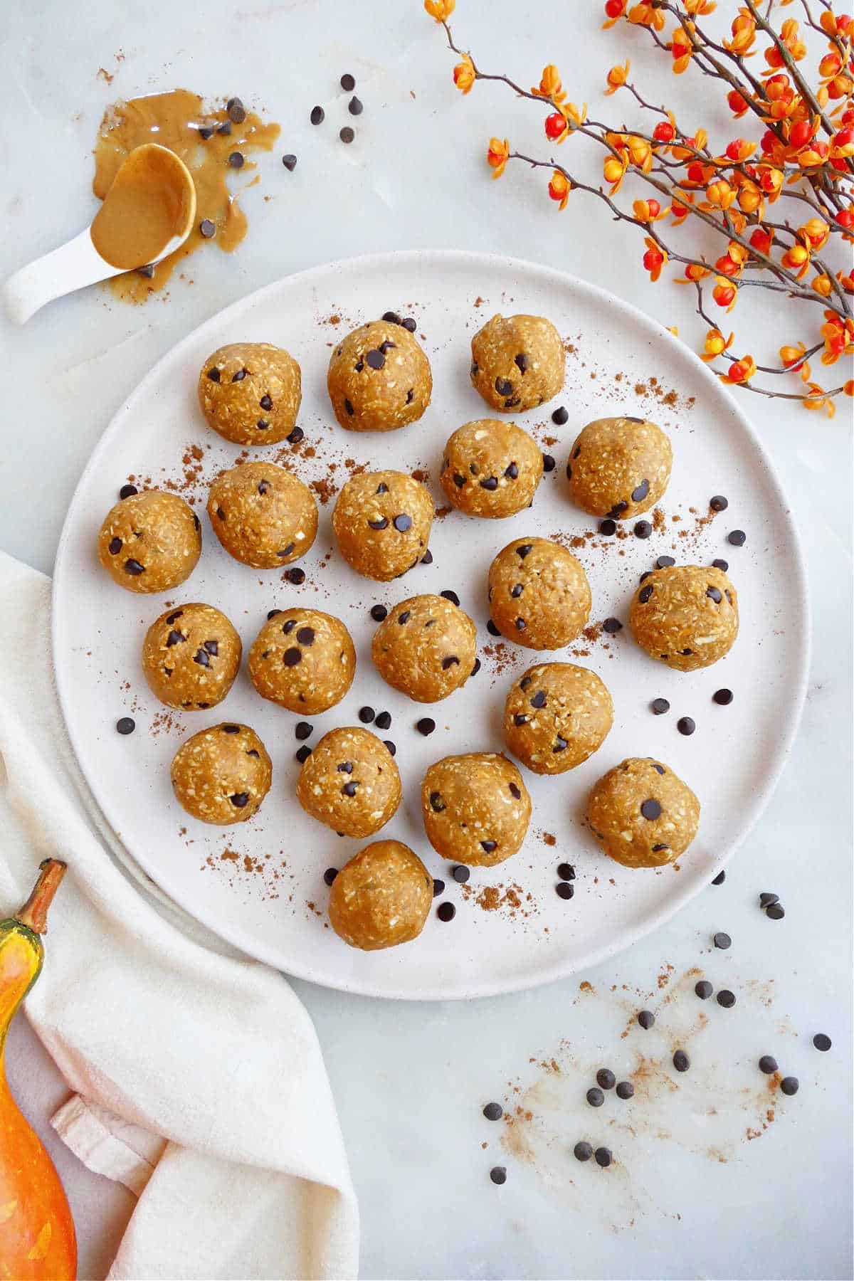 pumpkin peanut butter balls on a serving plate with chocolate chips surrounded by seasonal props