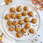 pumpkin peanut butter balls on a serving plate with chocolate chips surrounded by seasonal props