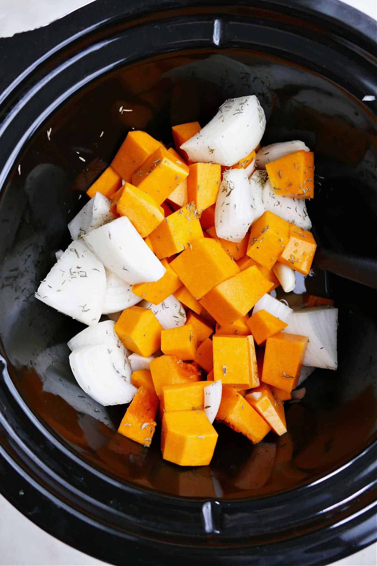 cubed butternut squash and chopped onions in a crockpot