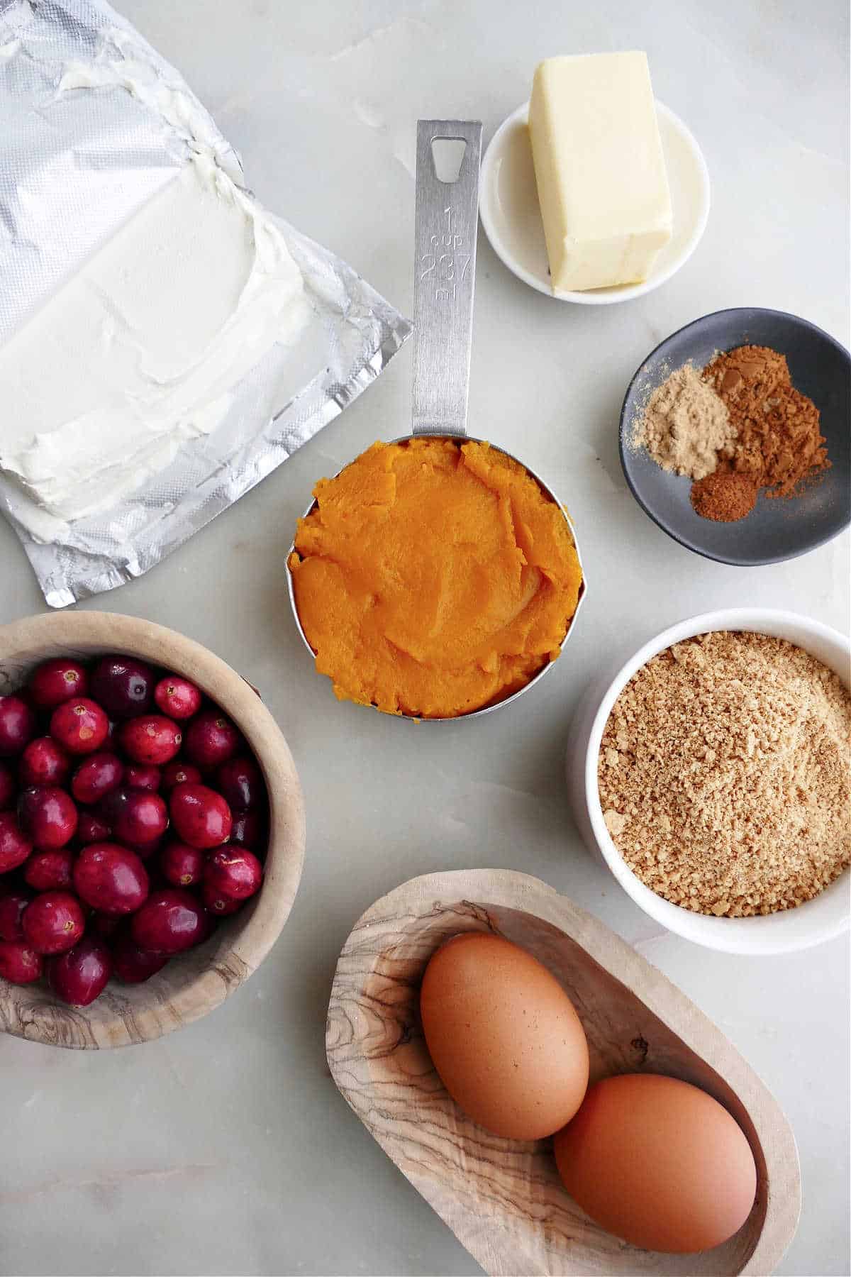 cream cheese, pumpkin, butter, spices, brown sugar, eggs, and cranberries on a counter