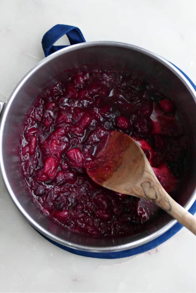 cranberries being cooked down in a saucepan with a wooden spoon