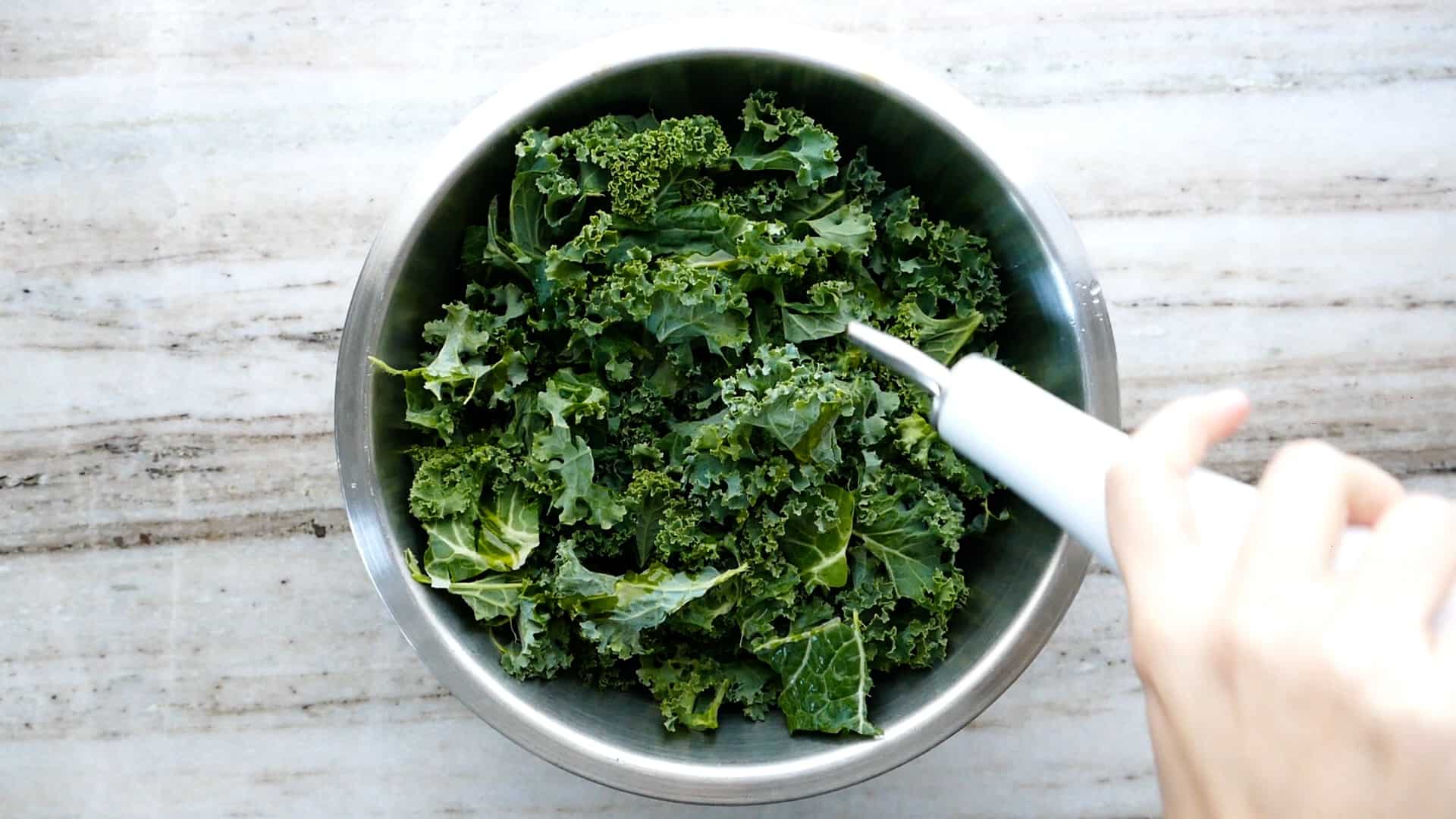 woman drizzling olive oil over a bowl of raw kale leaves on a counter