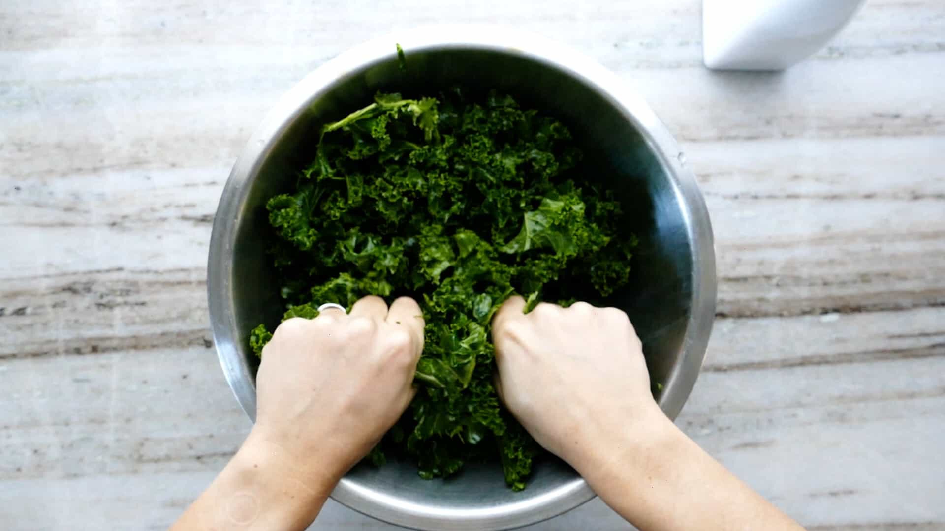 woman massaging raw kale leaves with oil and her hands in a mixing bowl