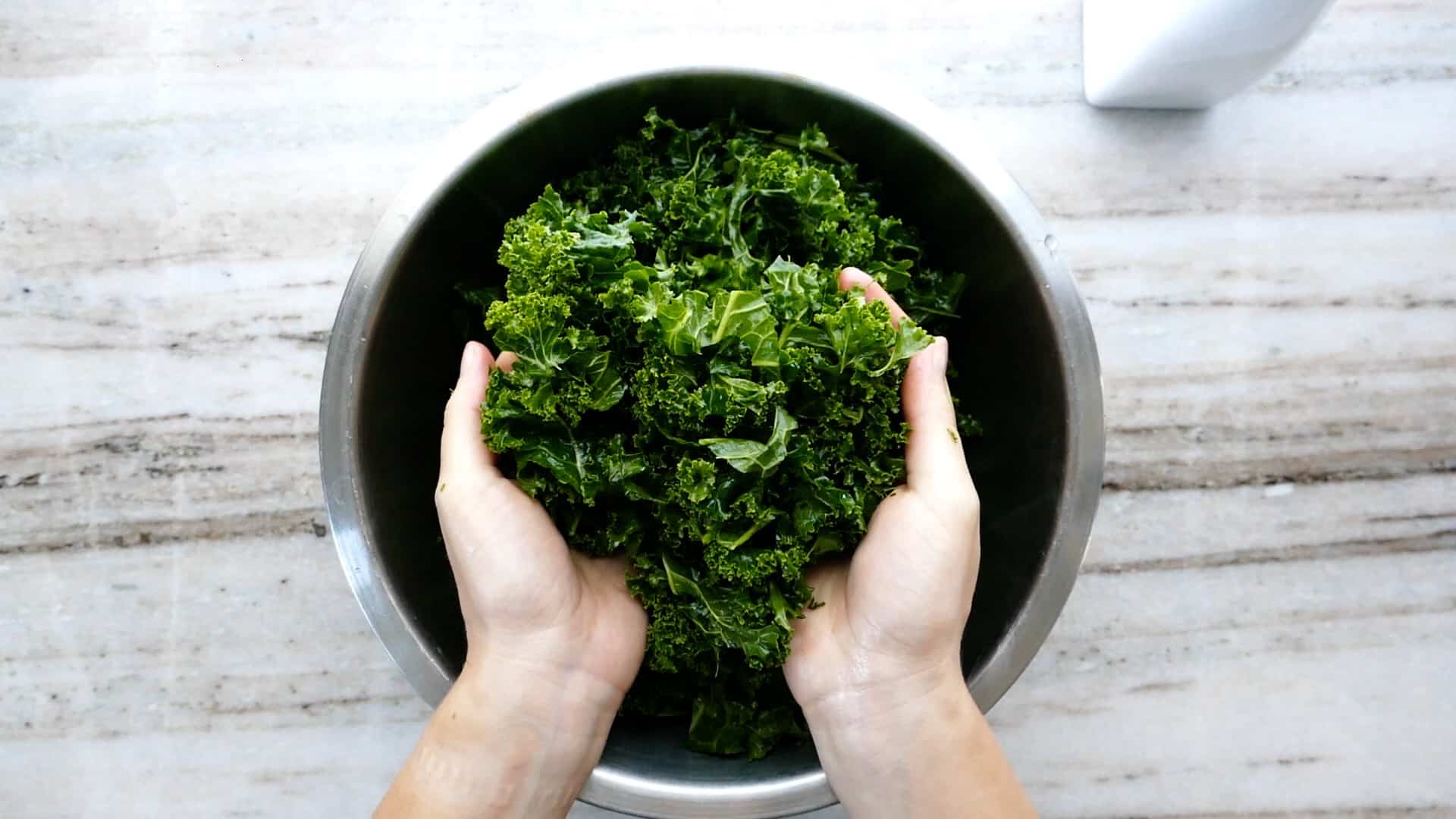 woman holding up massaged kale leaves in the palms of her hands