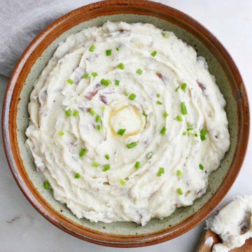 Instant Pot mashed red potatoes in a serving bowl topped with butter and sliced chives