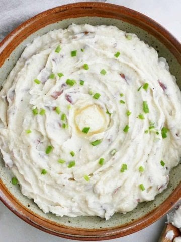 Instant Pot mashed red potatoes in a serving bowl topped with butter and sliced chives