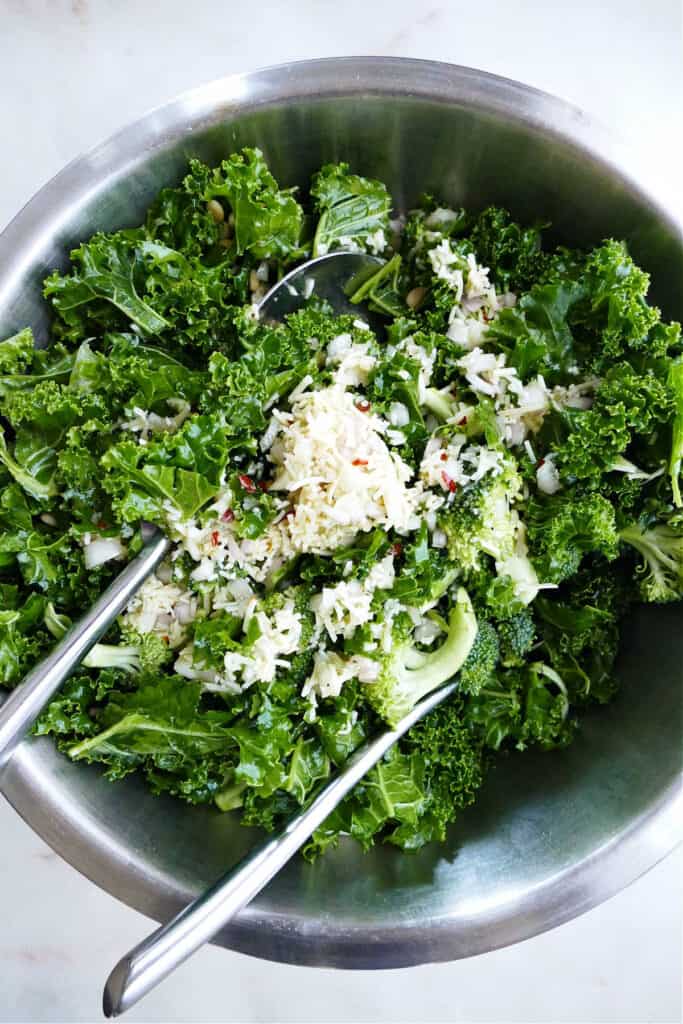 kale and broccoli salad being tossed in lemon parmesan dressing in a bowl