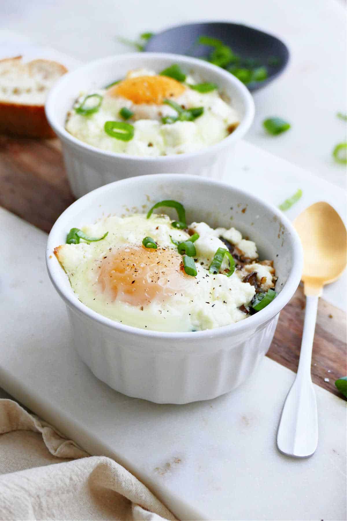 ramekin eggs topped with scallions on a serving tray next to a spoon