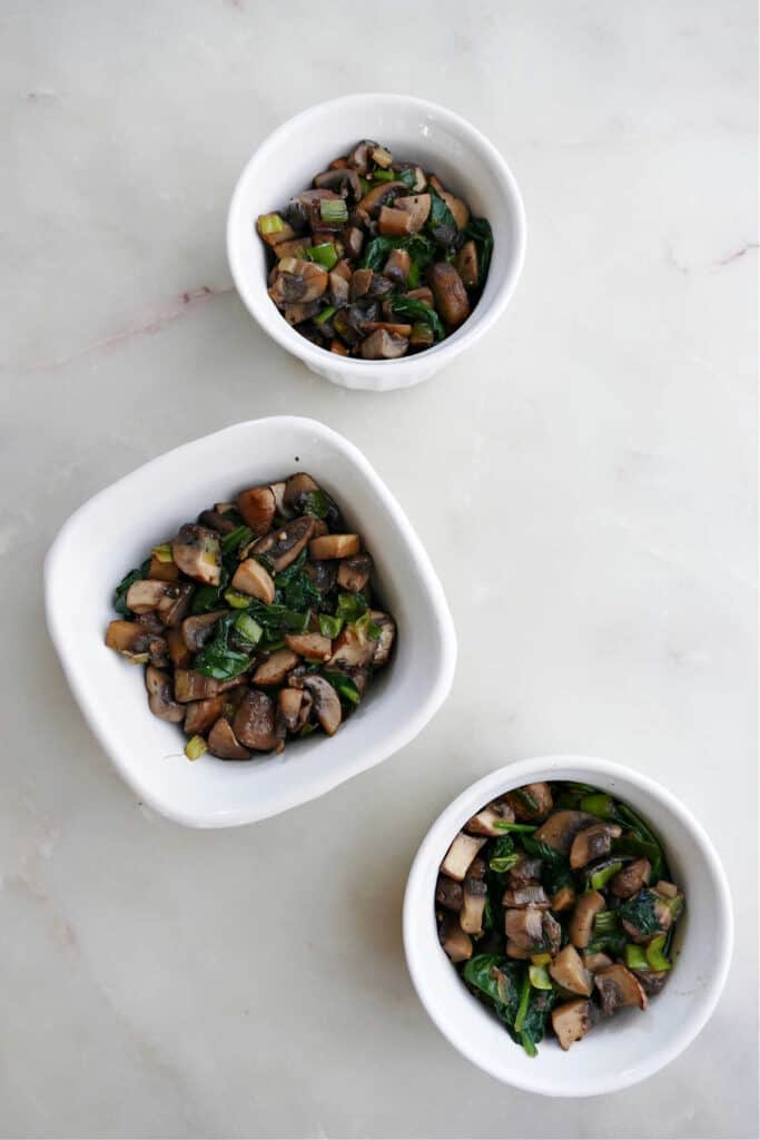 sauteed mushrooms and spinach divided between three ramekins on a counter