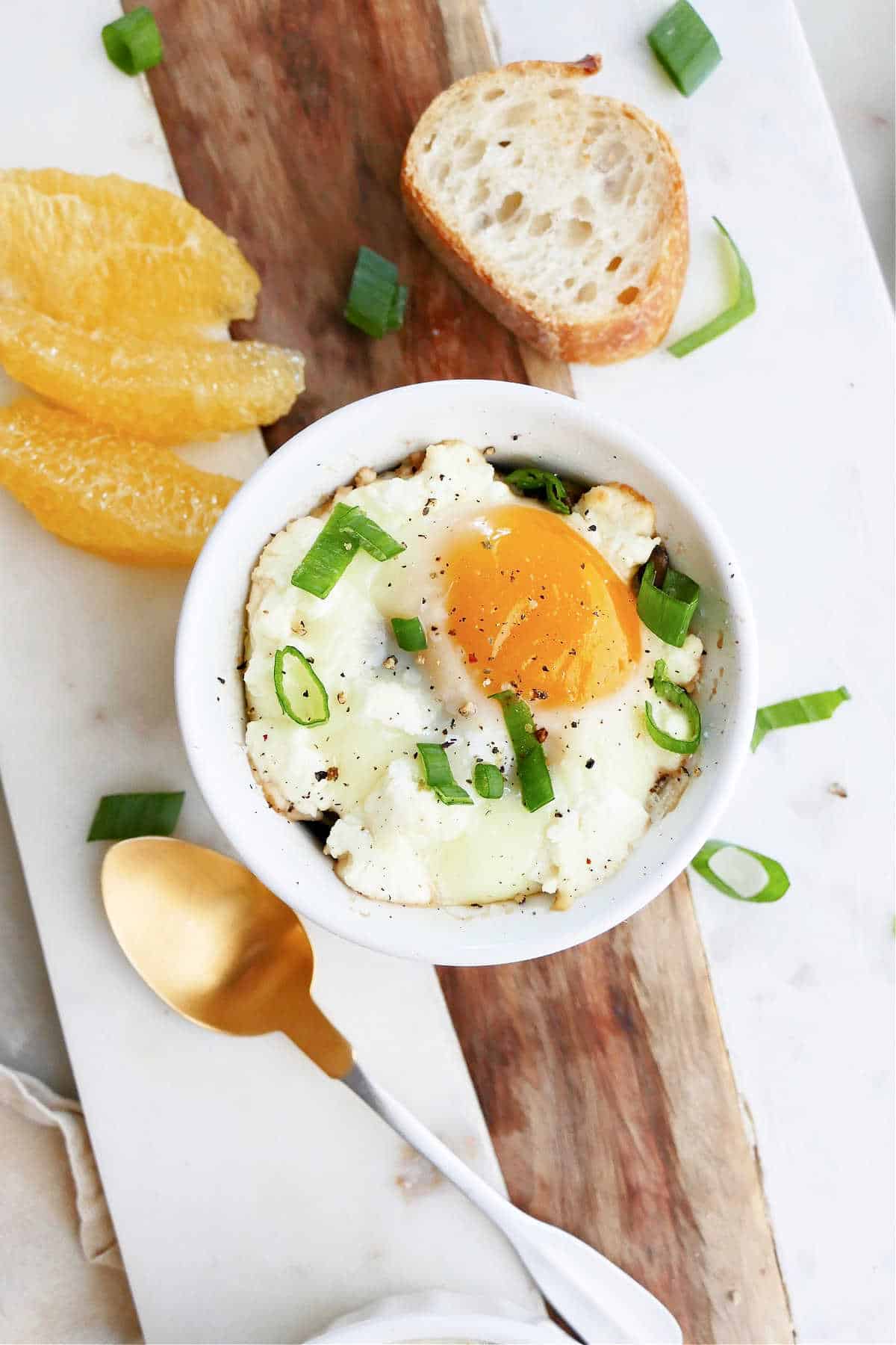 baked ramekin eggs topped with goat cheese and scallions next to fruit and bread