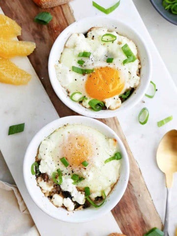 ramekin eggs with veggies on a serving board next to bread and fruit