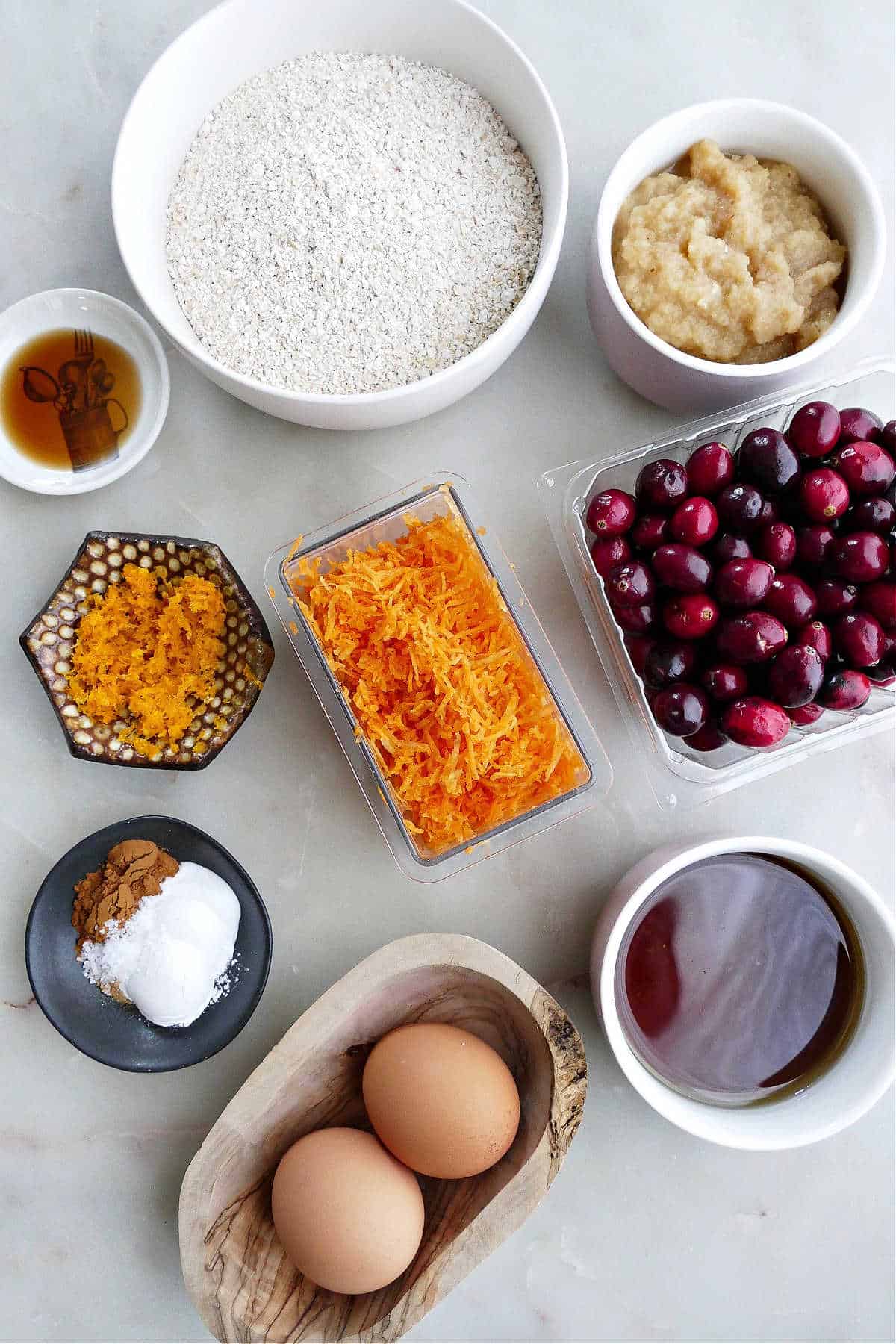 ground oats, applesauce, cranberries, grated carrots, orange zest, vanilla, spices, maple syrup, and eggs on a counter