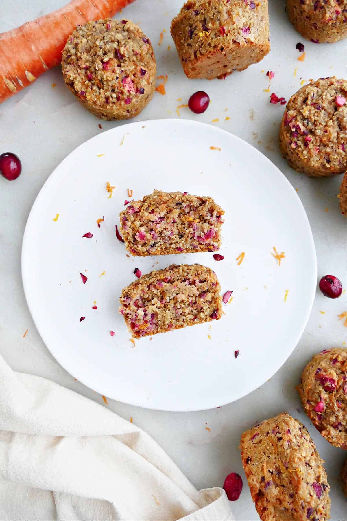 an orange carrot muffin with cranberries cut in half on a plate on a counter