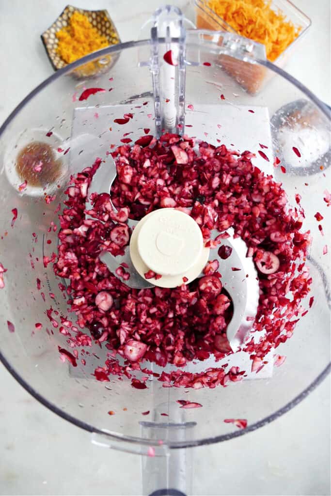fresh cranberries being chopped in a food processor with an S blade on a counter