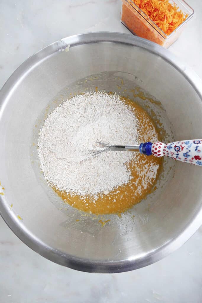 batter for orange carrot muffins in a mixing bowl with dry ingredients being folded into it