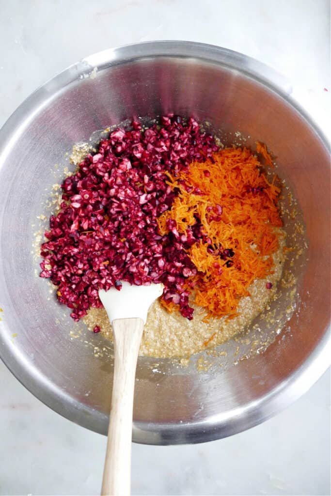 chopped cranberries and grated carrots folded into muffin batter in a bowl with a spatula