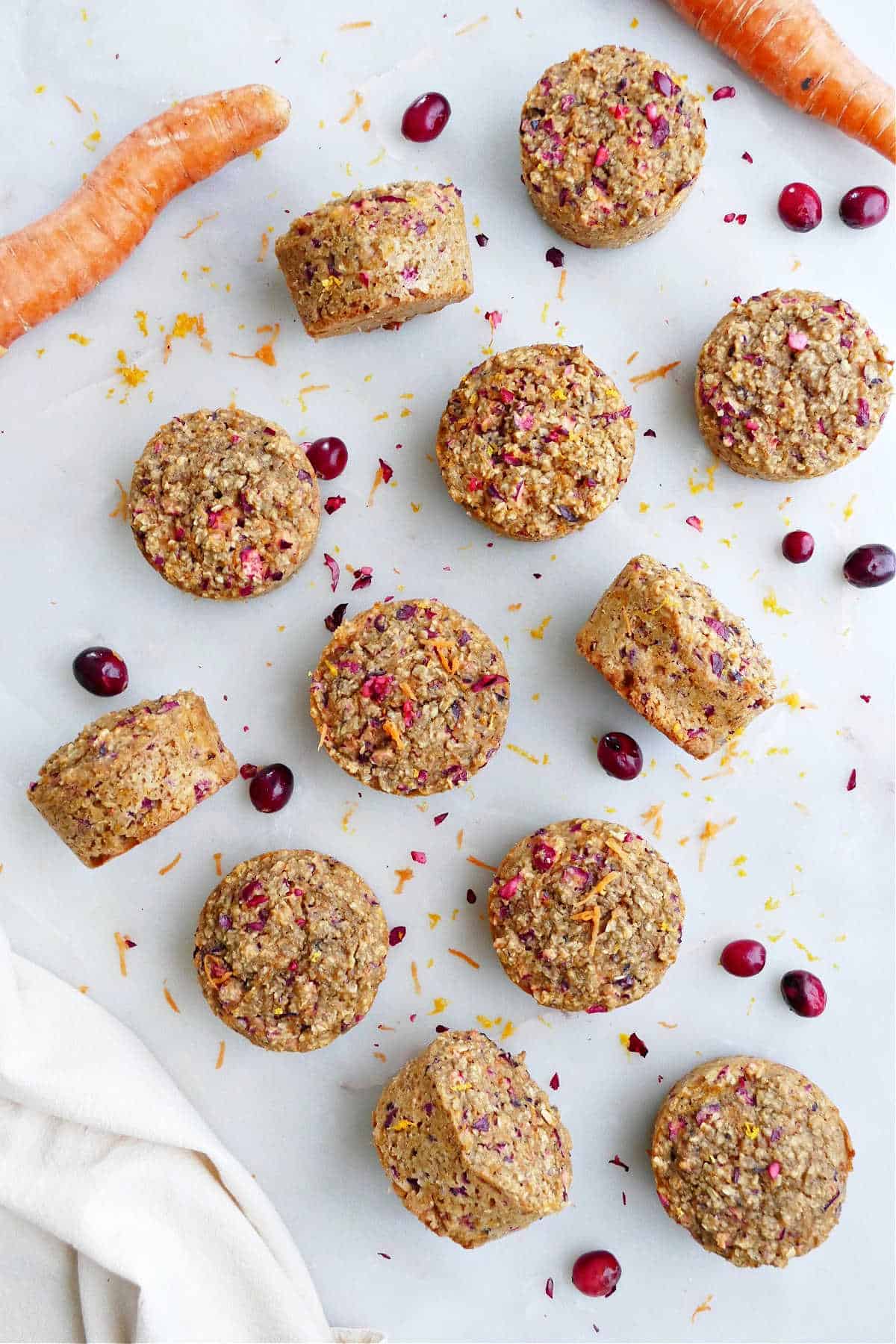 a dozen orange carrot muffins with cranberries on a counter next to each other
