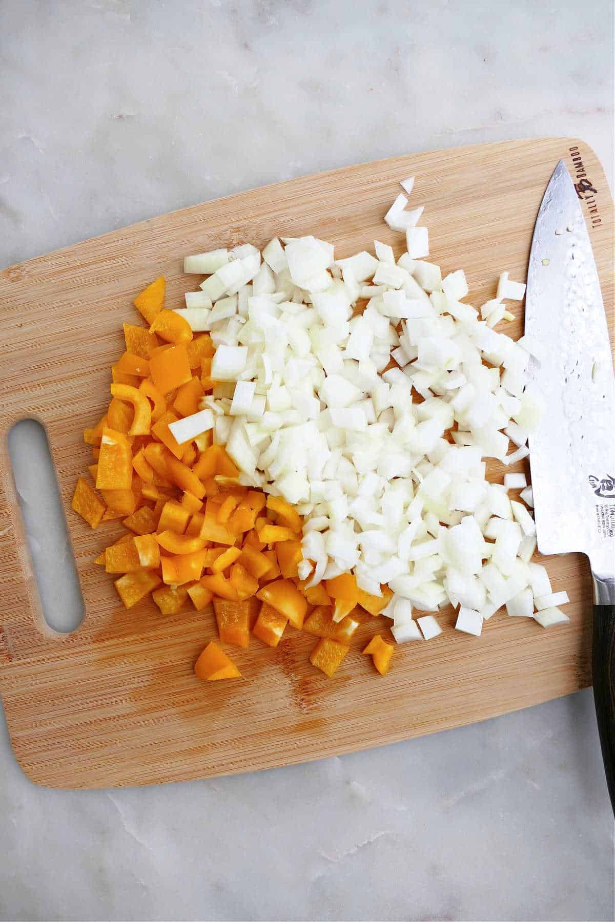diced bell pepper and yellow onion on a bamboo cutting board with chef's knife