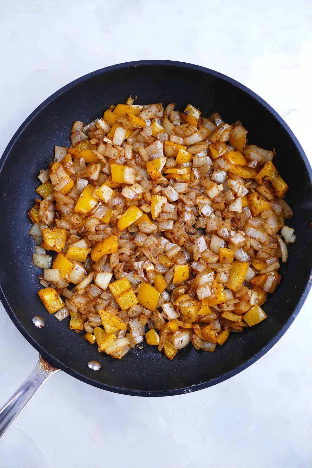 diced bell pepper and yellow onion with Mexican spices cooking in a skillet