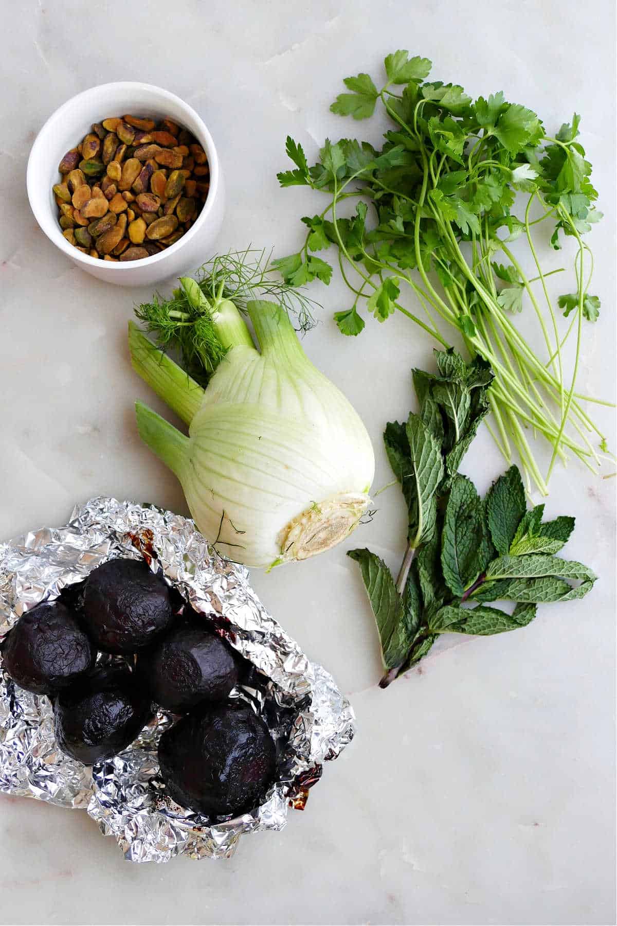 pistachios, fennel, parsley, mint, and roasted beets on a counter next to each other